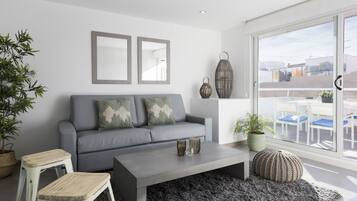 Una sala moderna con un sofá gris, dos espejos enmarcados, una mesa de centro y un ventanal con vistas al exterior.