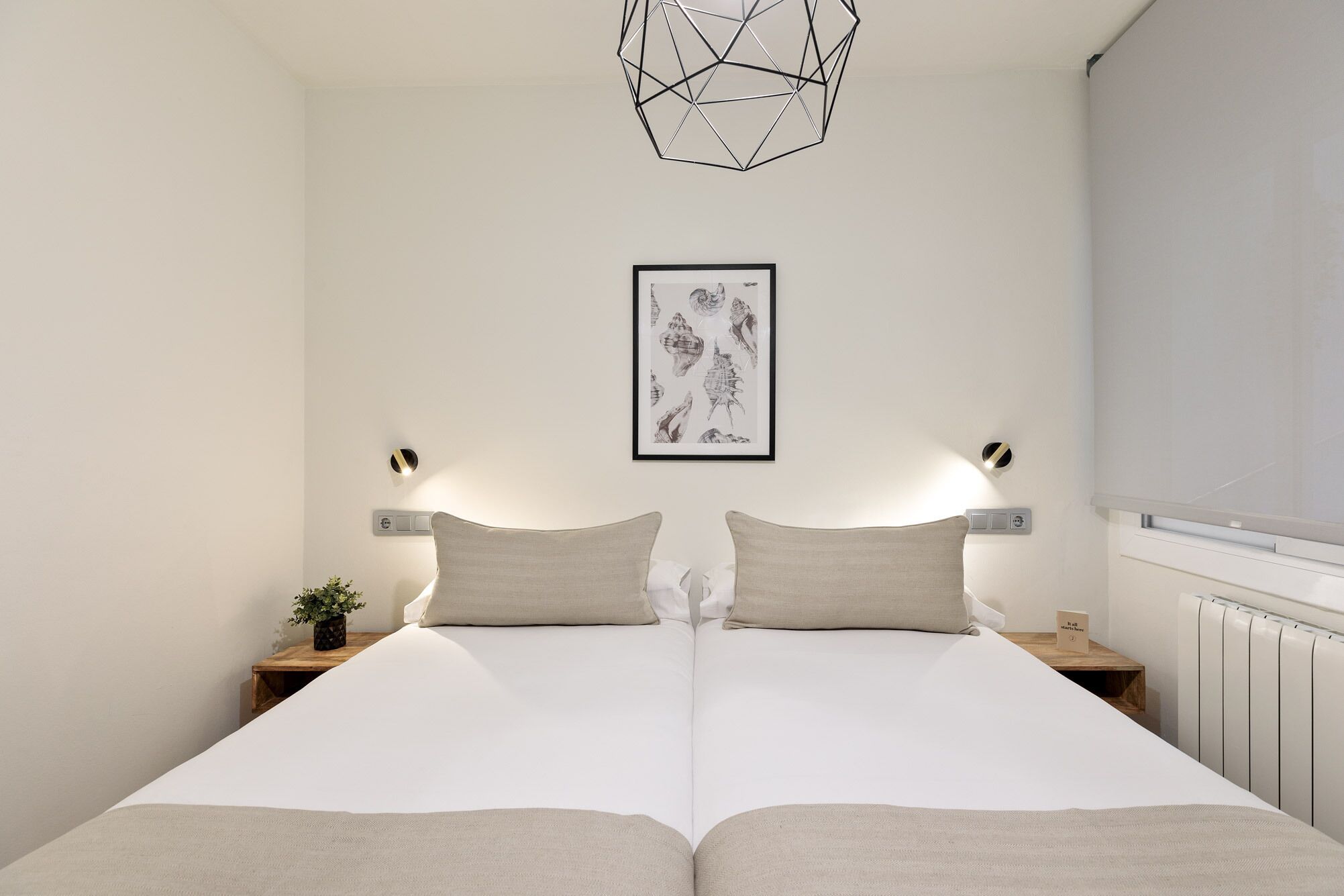 A modern bedroom with a large bed, two bedside tables, a wall-mounted light fixture, and a framed picture above the bed.