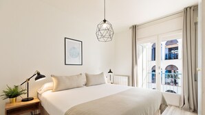Une chambre à coucher avec un grand lit, une table de chevet avec une lampe, un tableau encadré au mur et une fenêtre avec des rideaux.