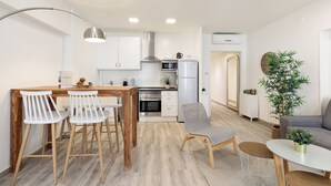 Une cuisine moderne avec des armoires blanches, un réfrigérateur en acier inoxydable et un four à micro-ondes. On y trouve également un coin repas avec une table en bois et des chaises blanches.