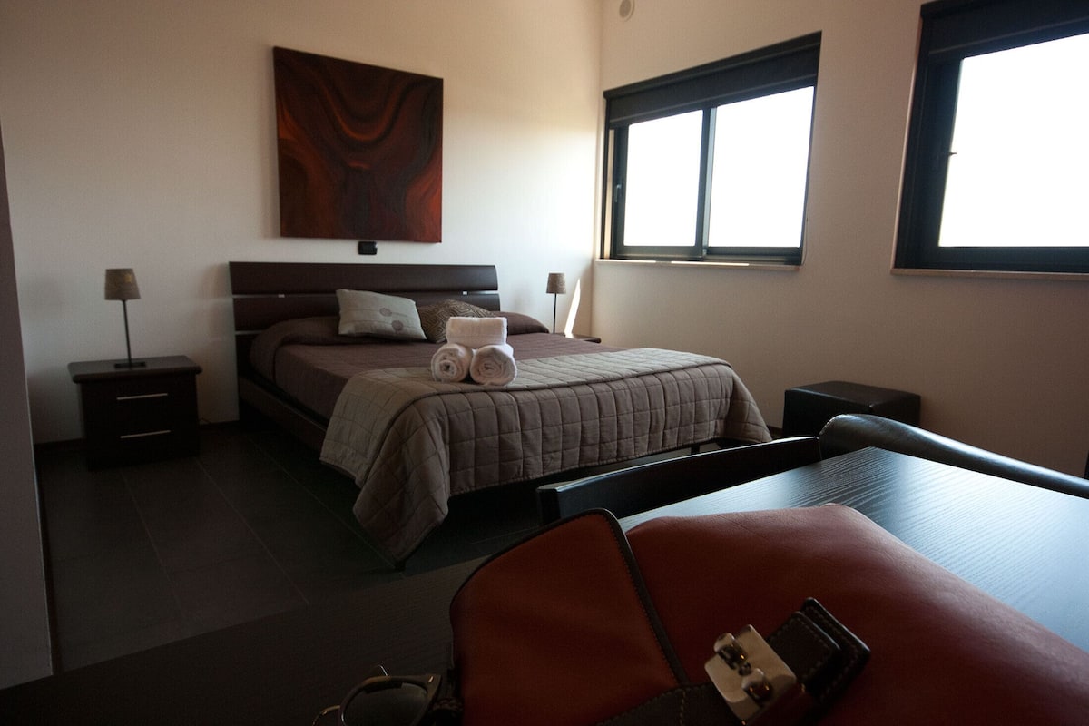 A hotel room with a bed, bedside tables, a desk, and a chair.