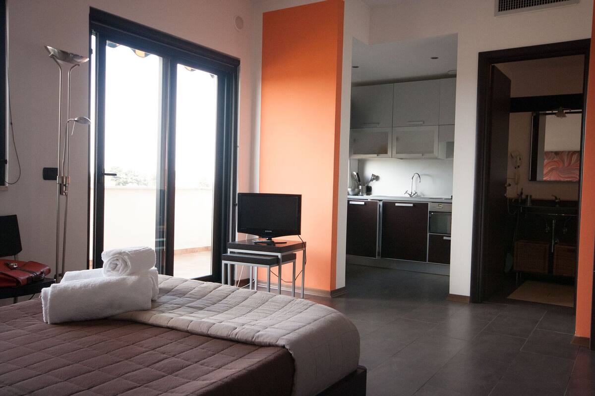 A hotel room with a bed, a TV, a desk, and a kitchenette.