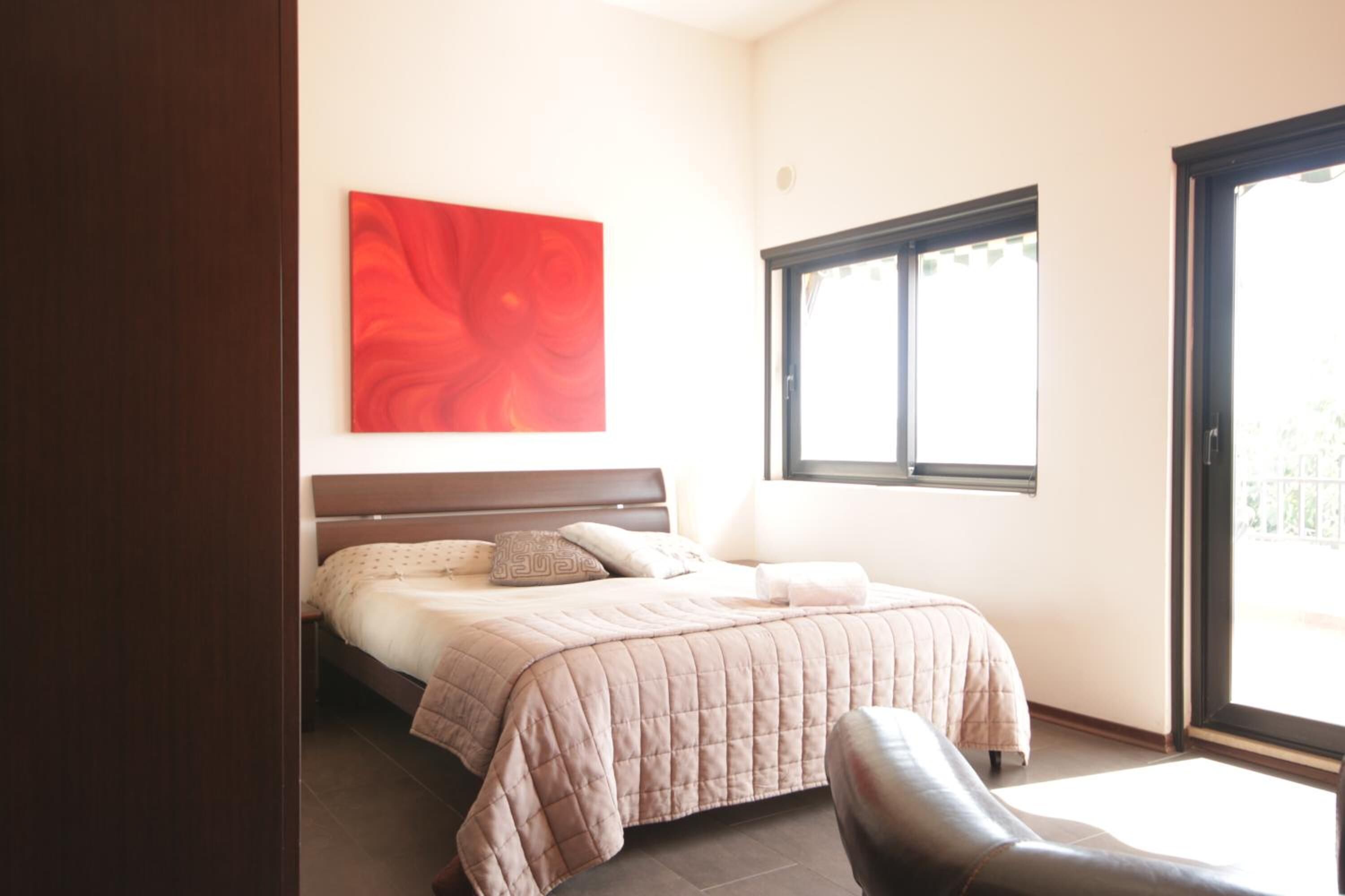 Ein Schlafzimmer mit einem Bett, einem großen Fenster und einem roten, abstrakten Gemälde an der Wand.