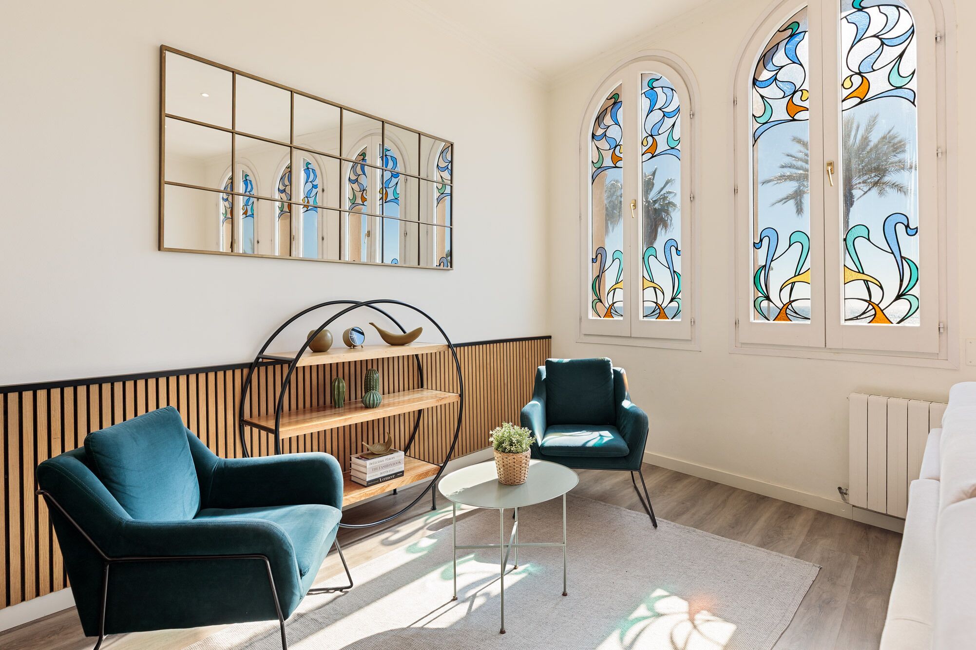 Una sala de estar moderna con sillones azul verdosos, una estantería de madera y un espejo grande.