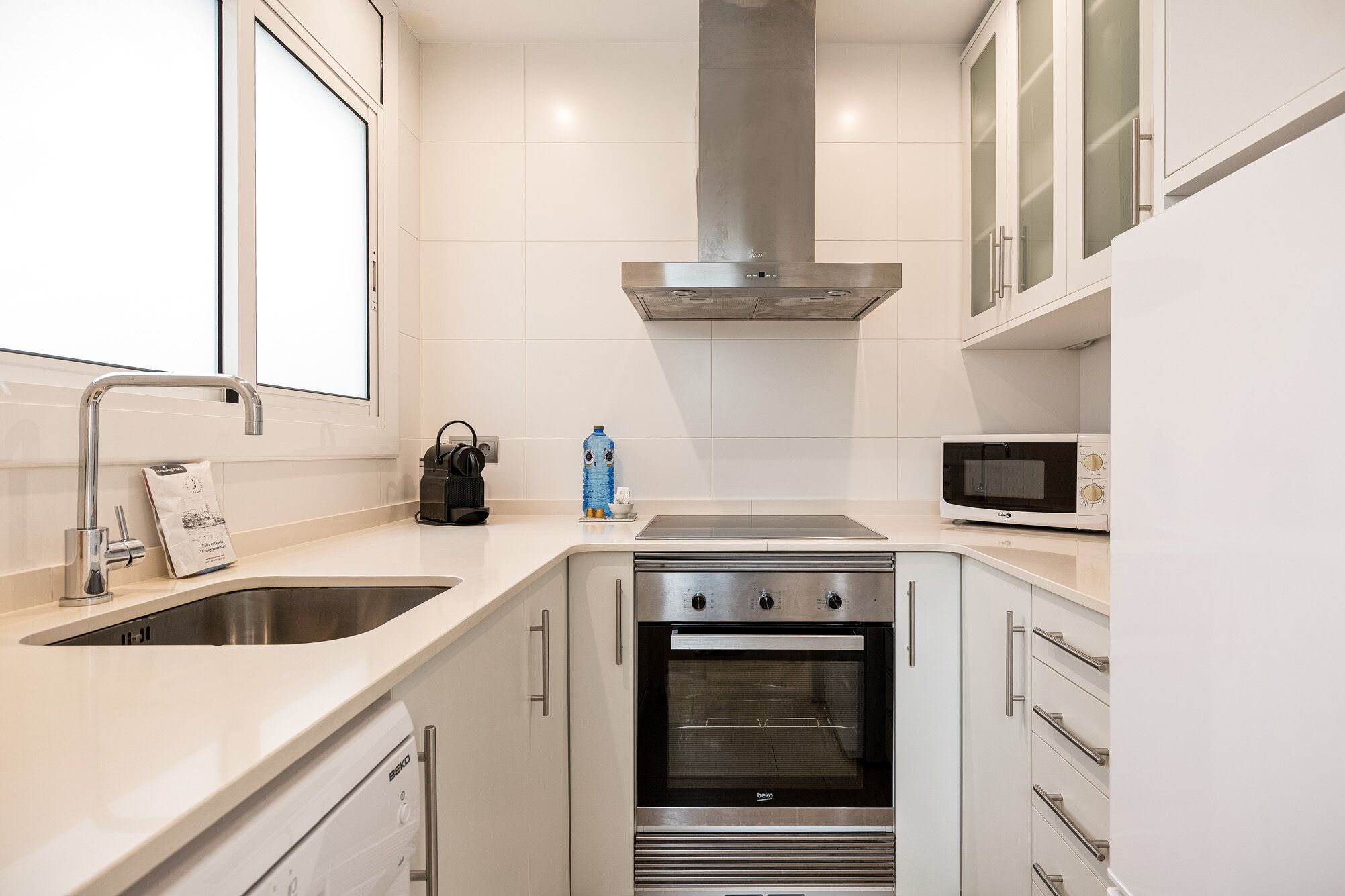 Una cocina compacta con un lavamanos de acero inoxidable, un horno empotrado y un microondas.