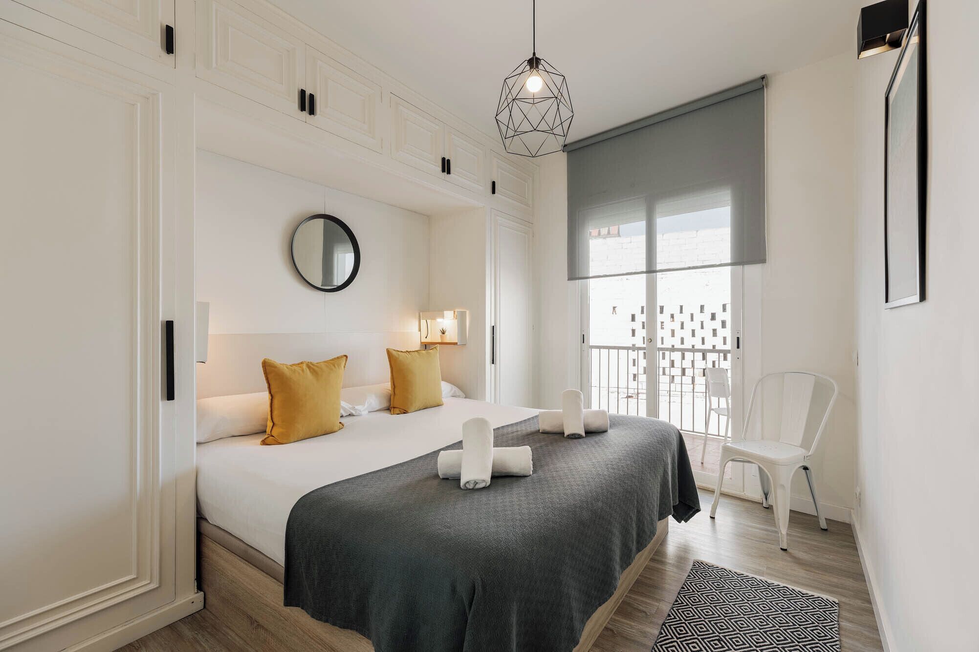Un dormitorio moderno con una cama grande, dos lámparas de noche, un espejo redondo y un balcón con vistas.