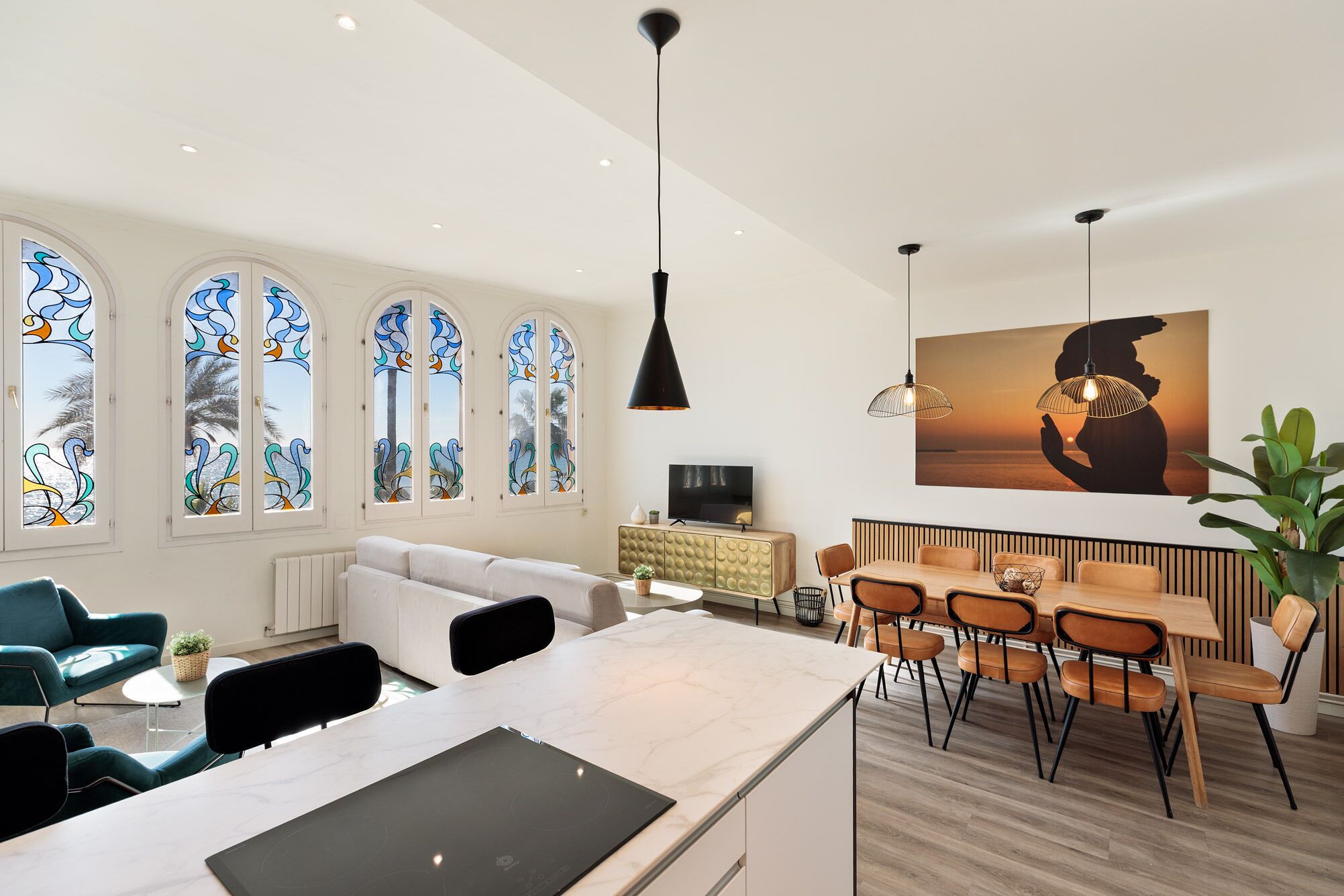 A modern living room with a white sofa, a dining area with wooden chairs, and large windows with stained glass.
