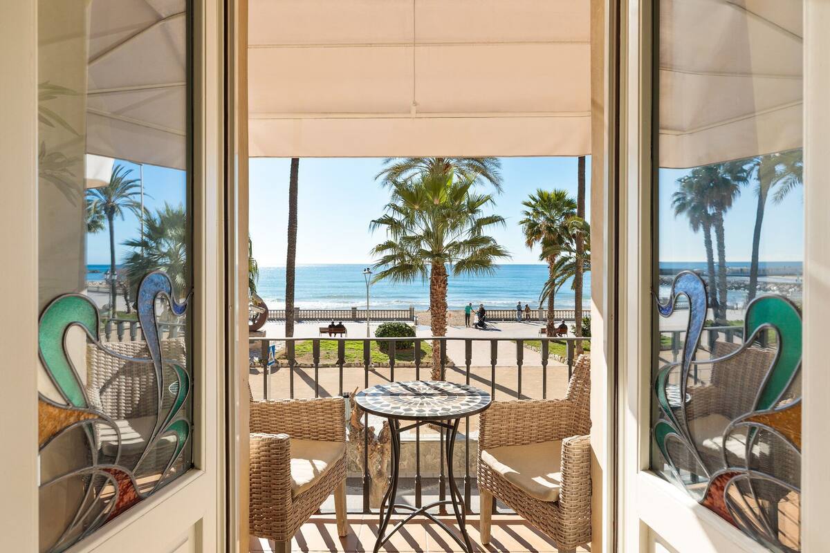 Een balkon met rieten meubilair, een tafeltje en uitzicht op het strand en de zee.