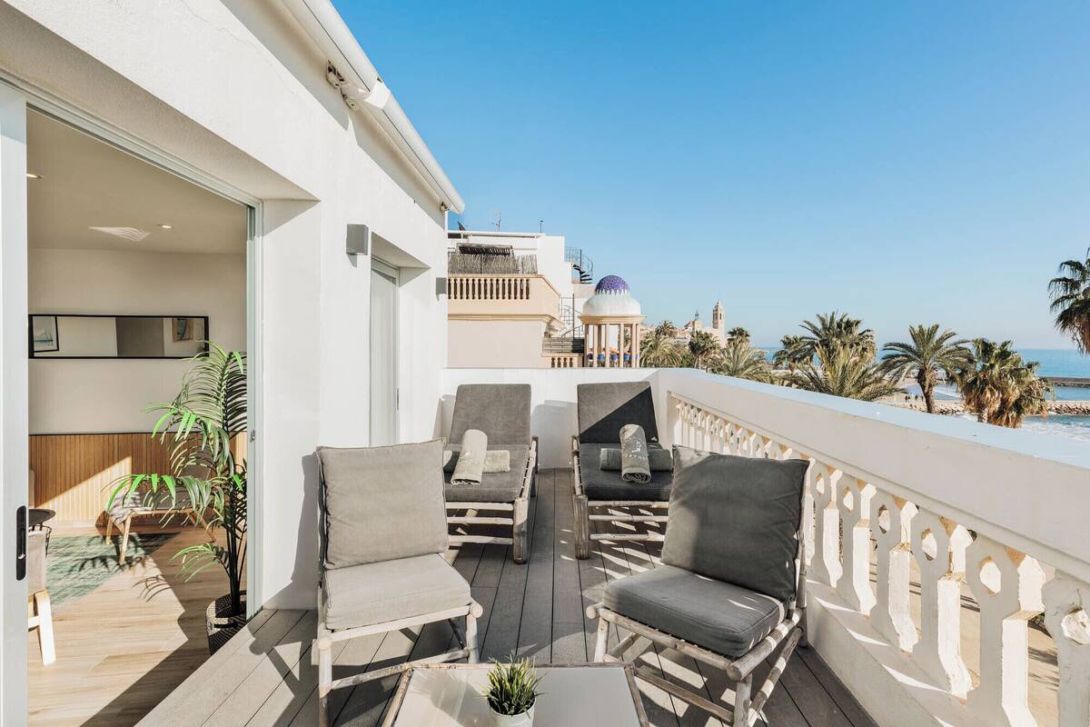 Een balkon met zitplaatsen, uitzicht op het strand en palmbomen.