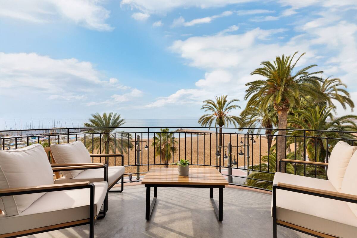 Een balkon met uitzicht op het strand, voorzien van zitplaatsen en een tafel.