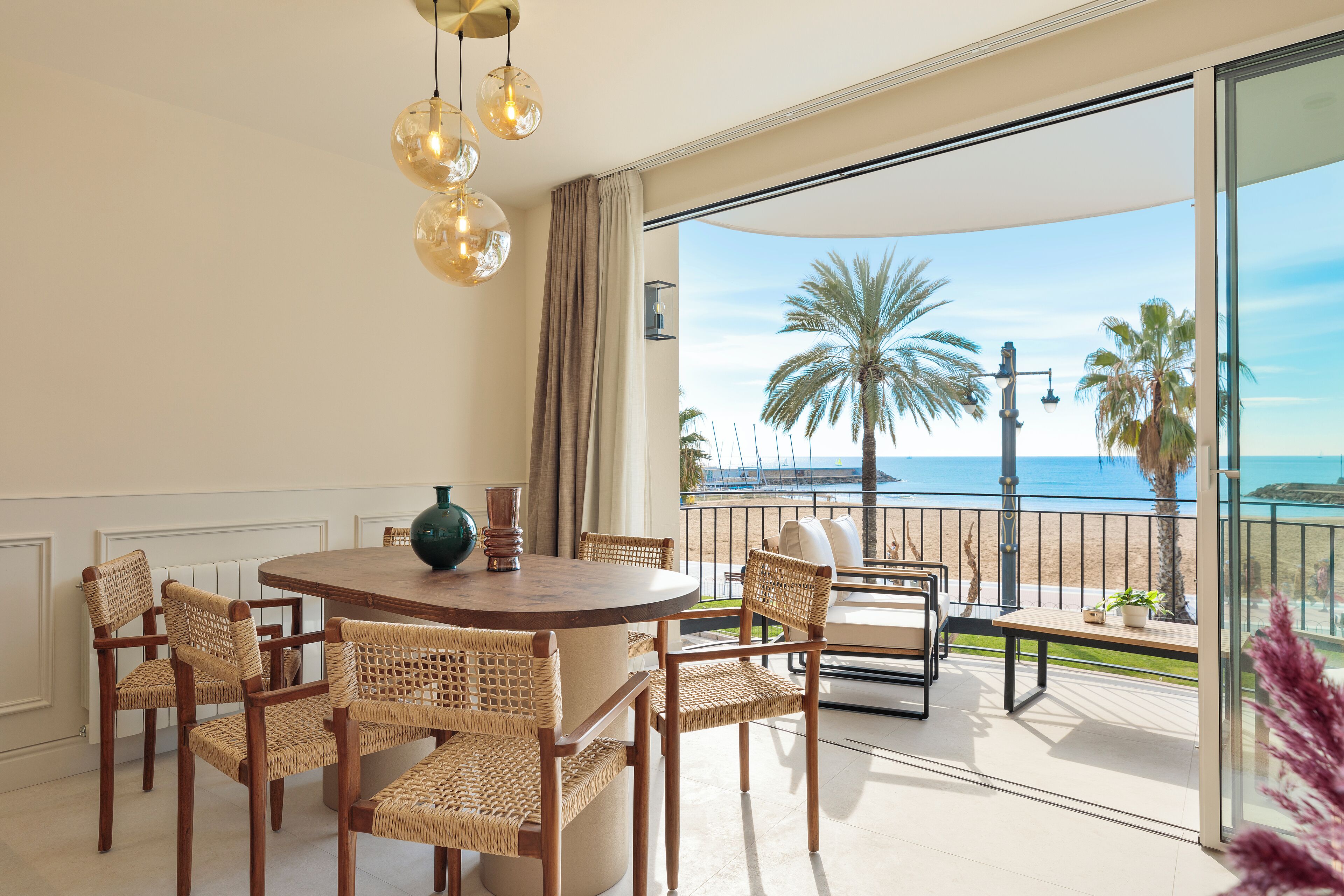 Un balcon avec vue sur la mer, des meubles en osier et une table ronde.