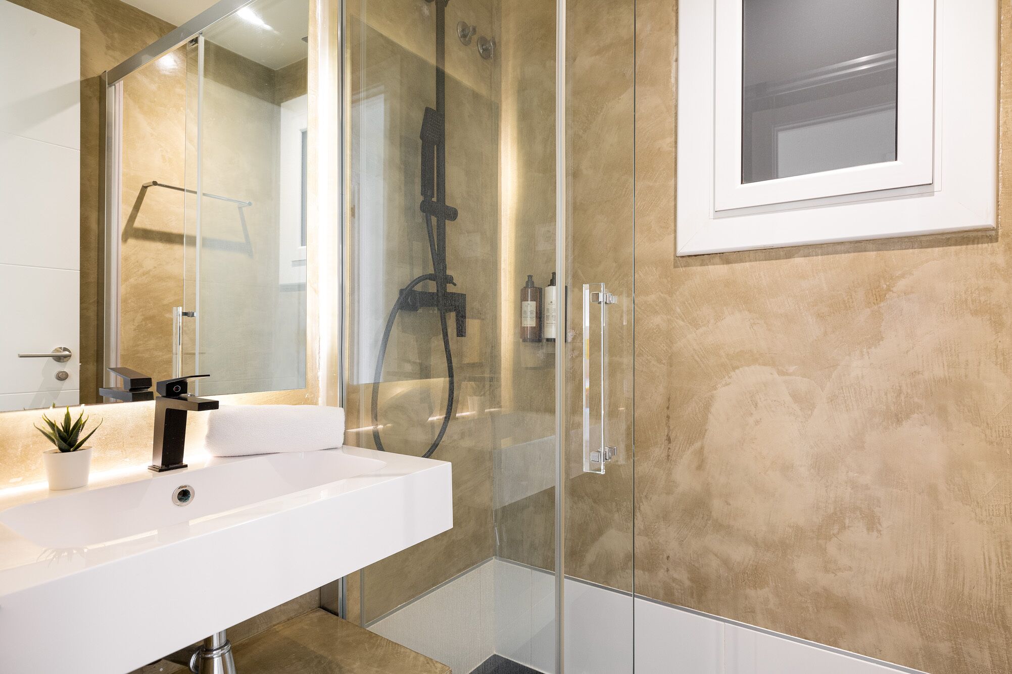 Een moderne badkamer met een douchecabine van glas, een witte wastafel en een spiegel.