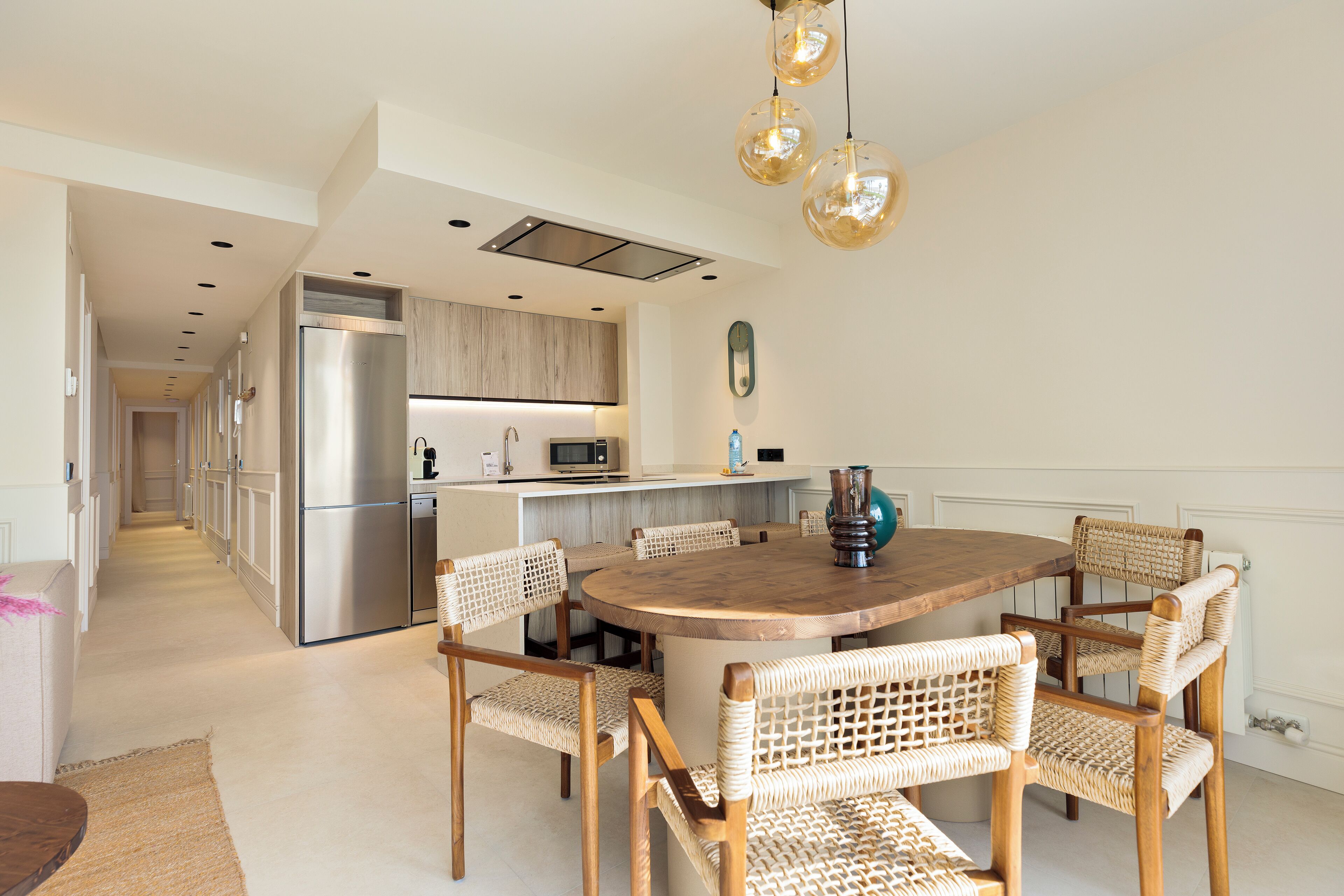 Una cocina moderna con un refrigerador de acero inoxidable, un microondas y una mesa de comedor de madera rodeada de sillas de mimbre.