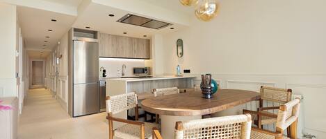 Una cocina moderna con un refrigerador de acero inoxidable, un microondas y una mesa de comedor de madera rodeada de sillas de mimbre.