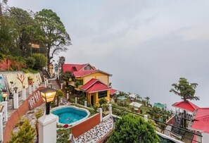 A hillside property with a swimming pool, a staircase leading to a house, and a view of the surrounding landscape.