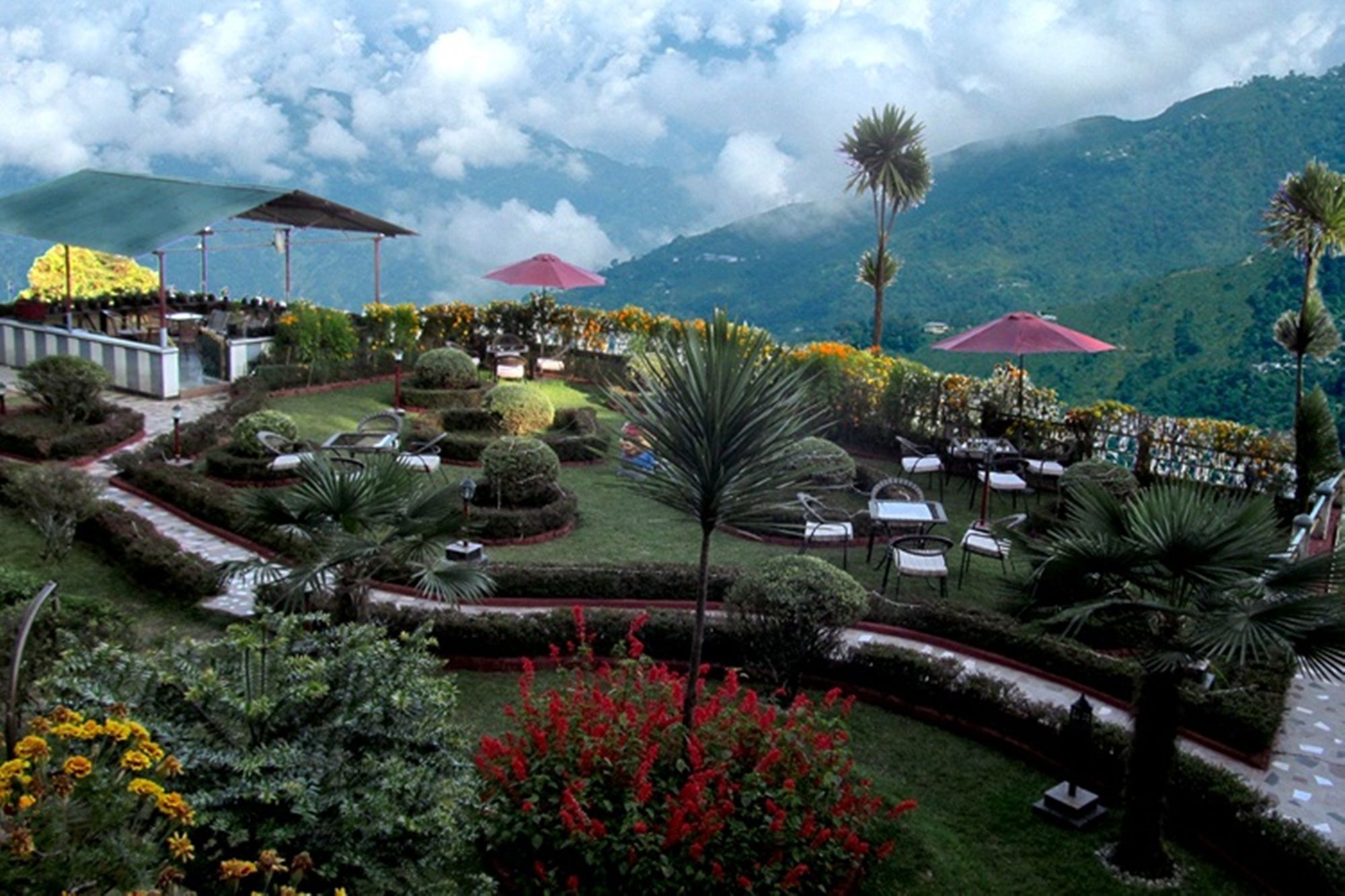 A landscaped garden with seating areas and umbrellas, surrounded by lush greenery and mountains.