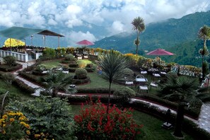 A landscaped garden with seating areas and umbrellas, surrounded by lush greenery and mountains.