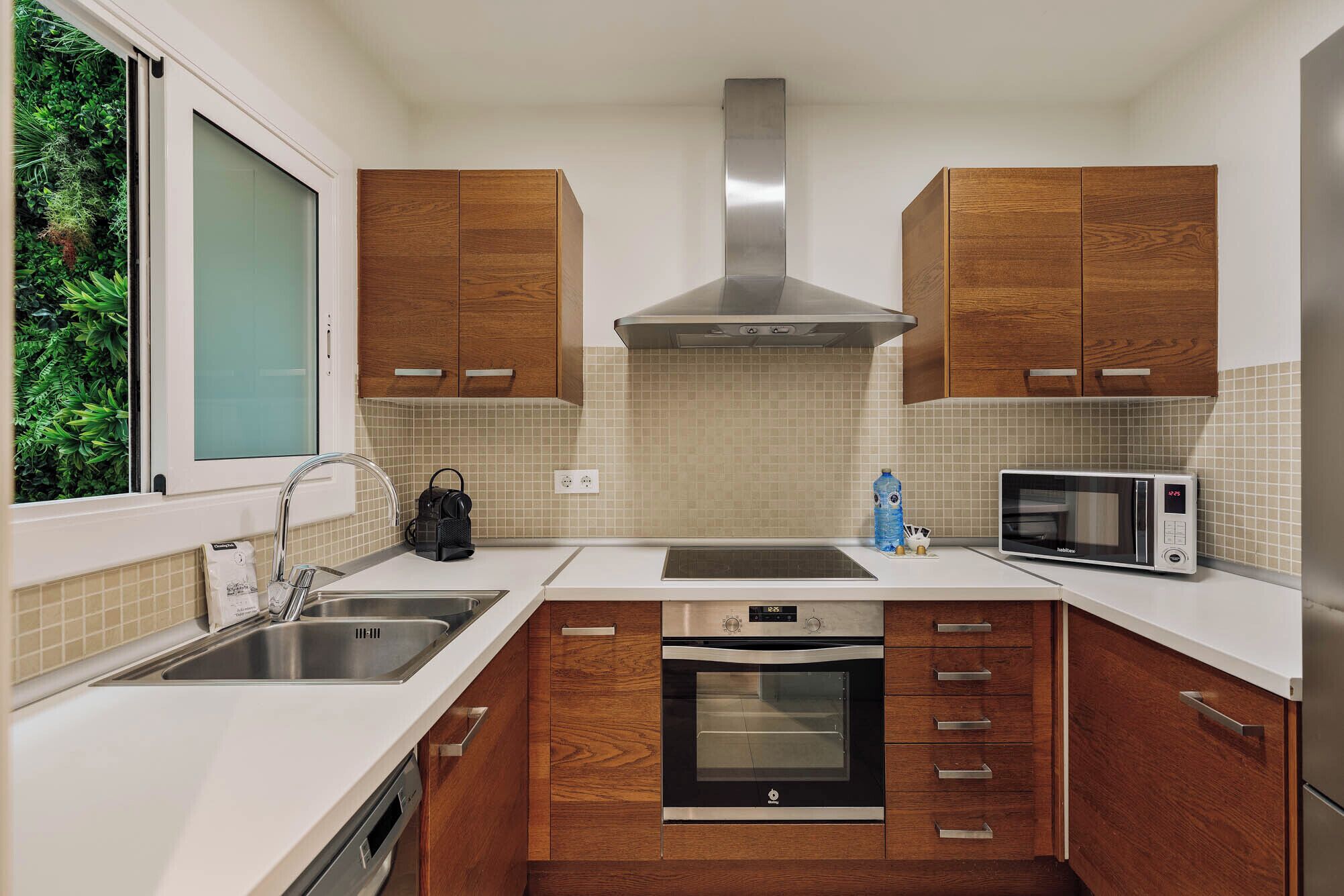 A compact kitchen with wooden cabinets, a stainless steel sink, a microwave, and an oven.