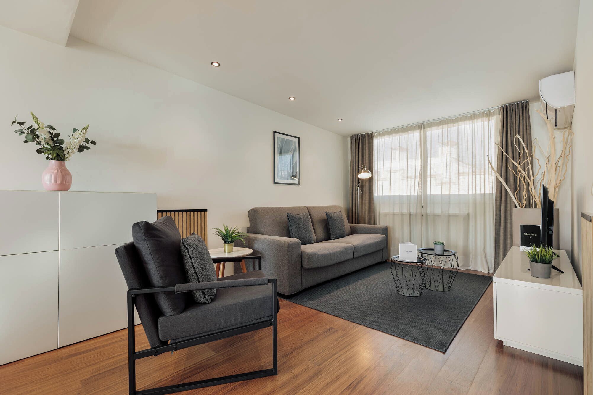 Una sala moderna con un sofá, un sillón y una mesita de noche con una lámpara.
