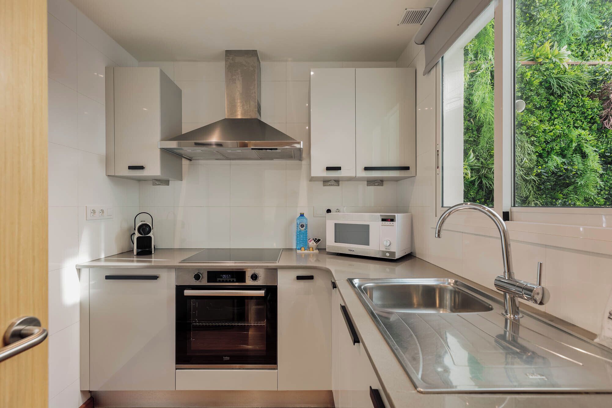 Une cuisine moderne avec des armoires blanches, une hotte de cuisinière en acier inoxydable, un four encastré, un four à micro-ondes et un évier avec un robinet.