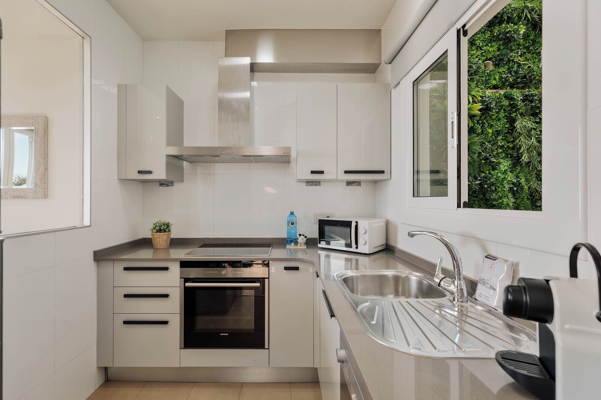 A modern kitchen with white cabinetry, a built-in oven, a microwave, and a stainless steel sink.