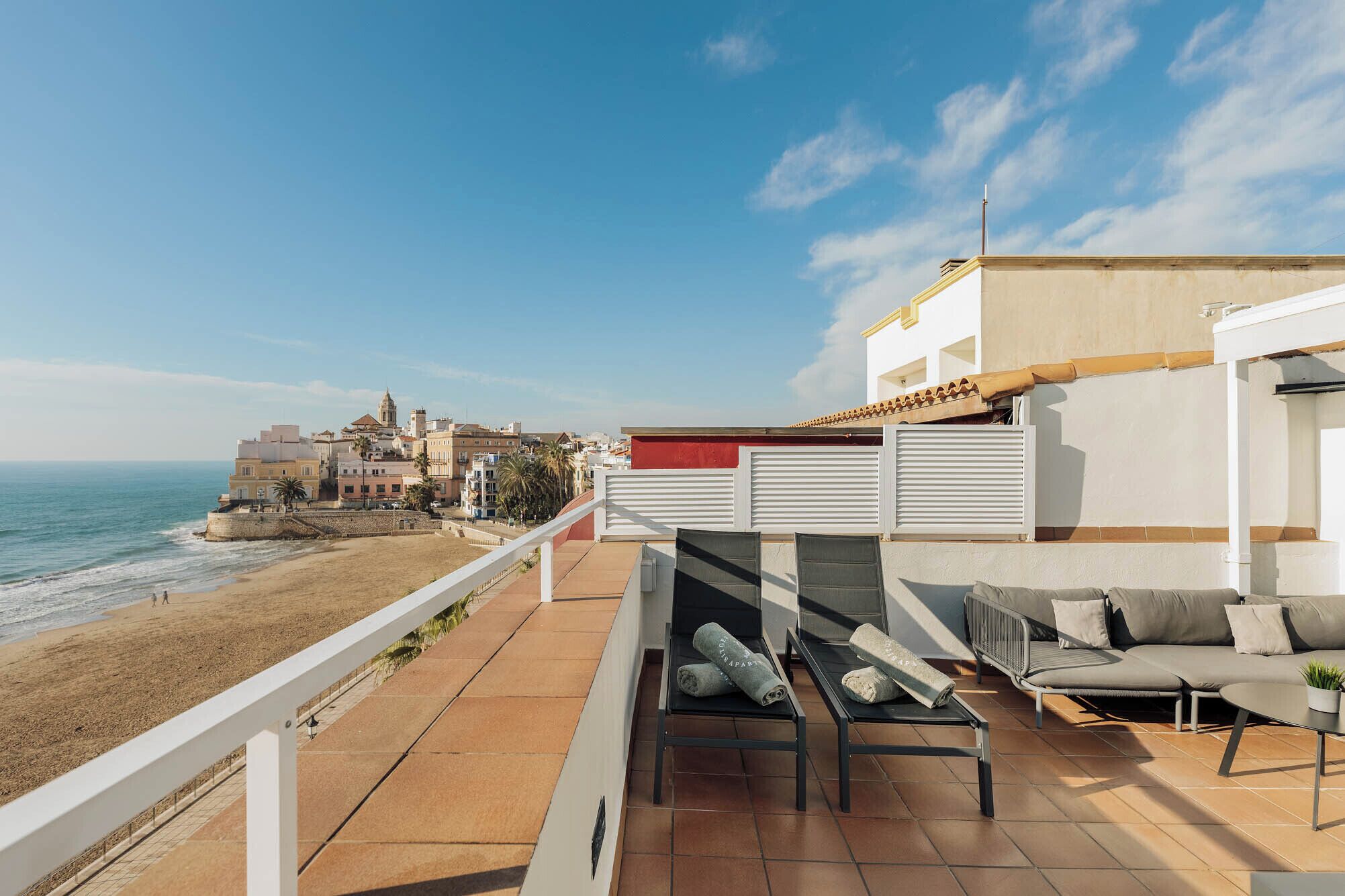 A balcony with a sofa, a table, and a view of the beach and ocean.