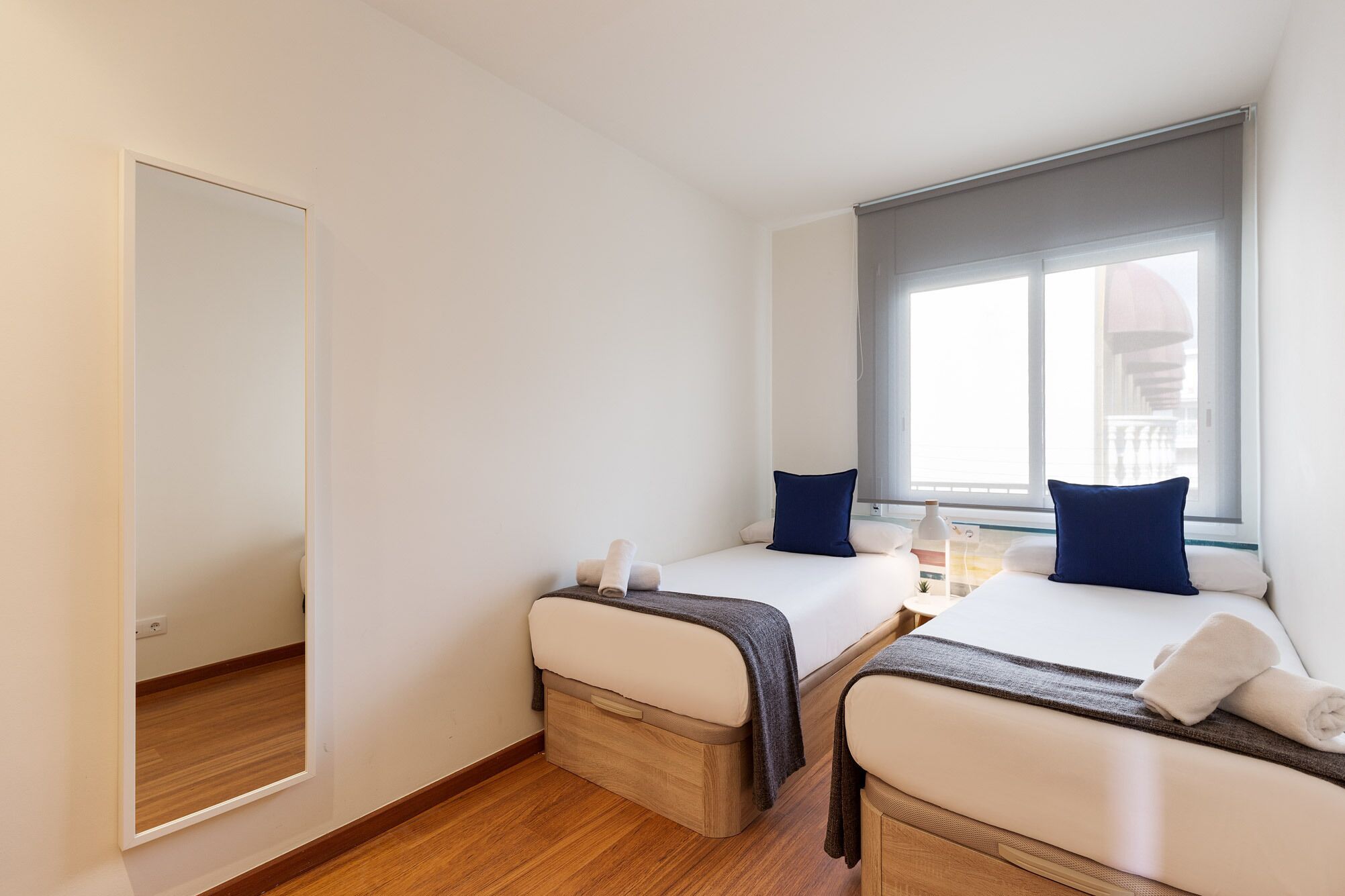 A bedroom with two beds, a large window, and a mirror.