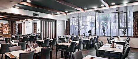 Un restaurante moderno con varias mesas y sillas, ventanas amplias y una decoración interior contemporánea.