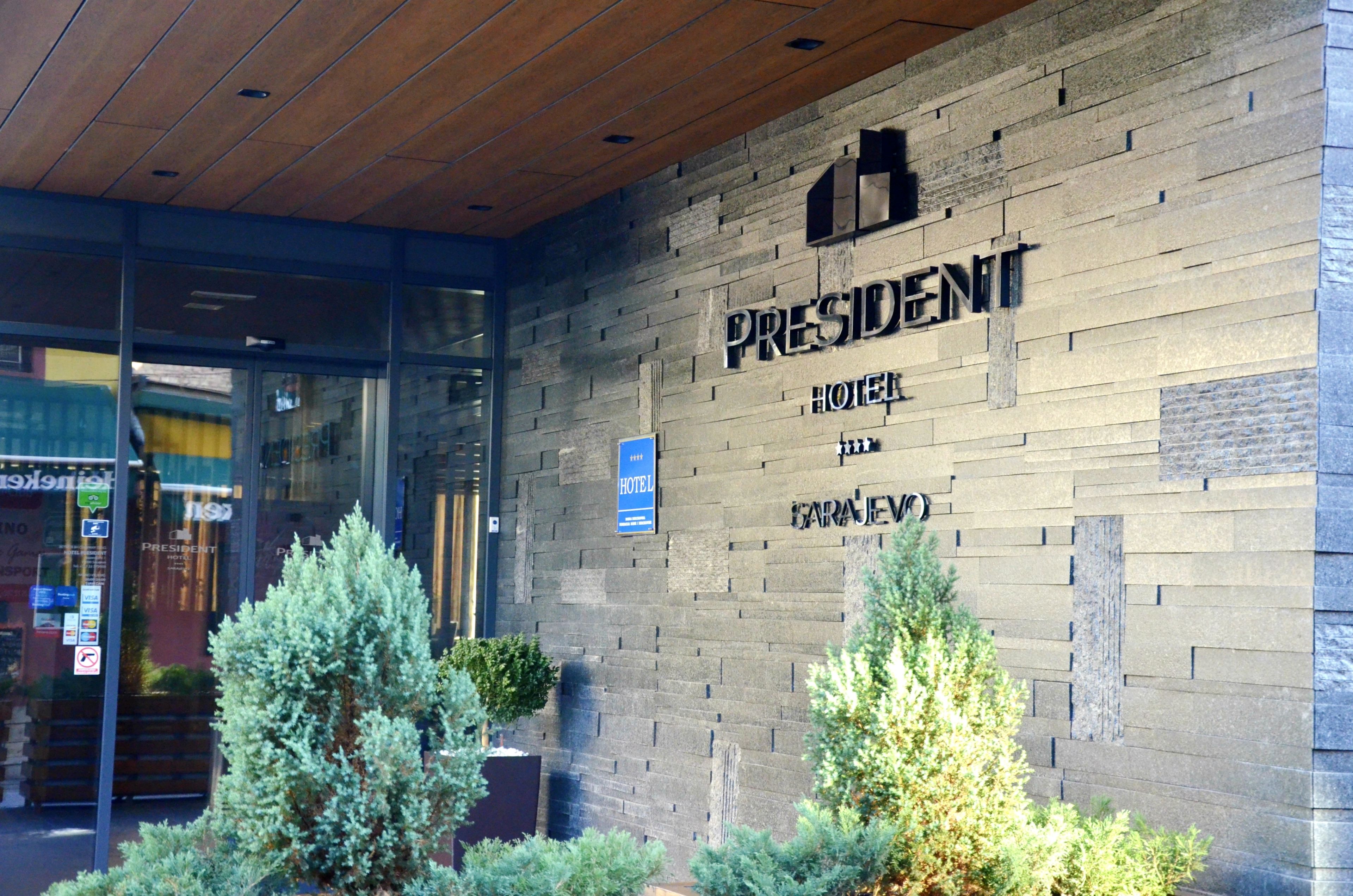 A hotel entrance with a stone facade, a sign reading "President Hotel," and a blue sign indicating "Hotel."