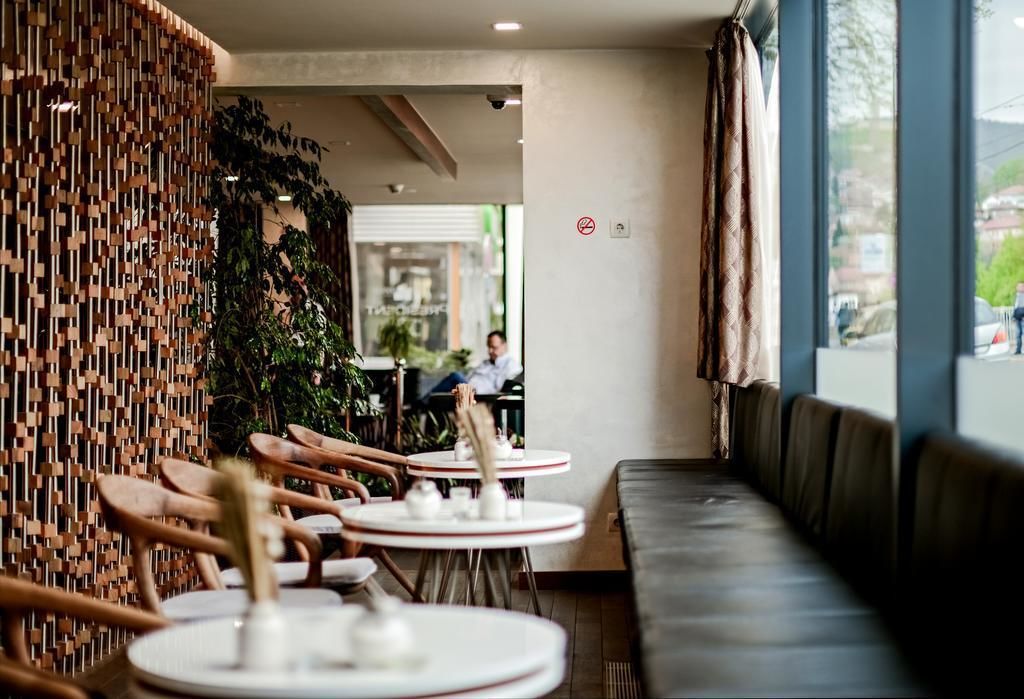 Un café moderne avec des tables rondes et des chaises en bois, un mur végétal et une vue sur la rue.