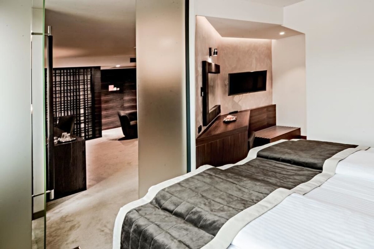 A modern hotel room with a bed, a TV mounted on the wall, and a desk with a chair.