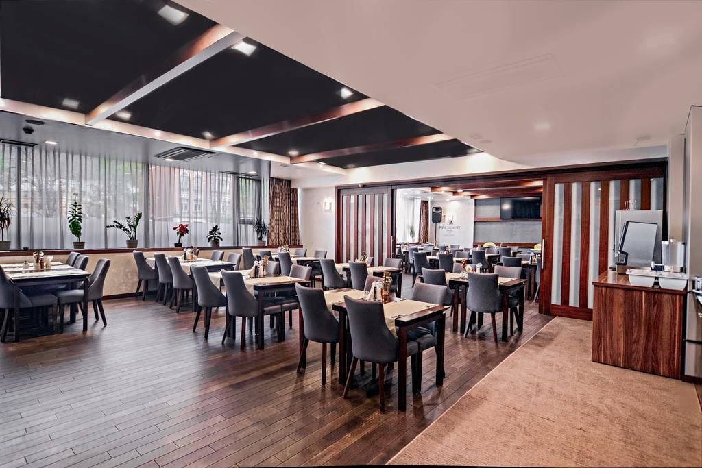 A spacious restaurant with multiple dining tables and chairs, a wooden floor, and a modern ceiling design.