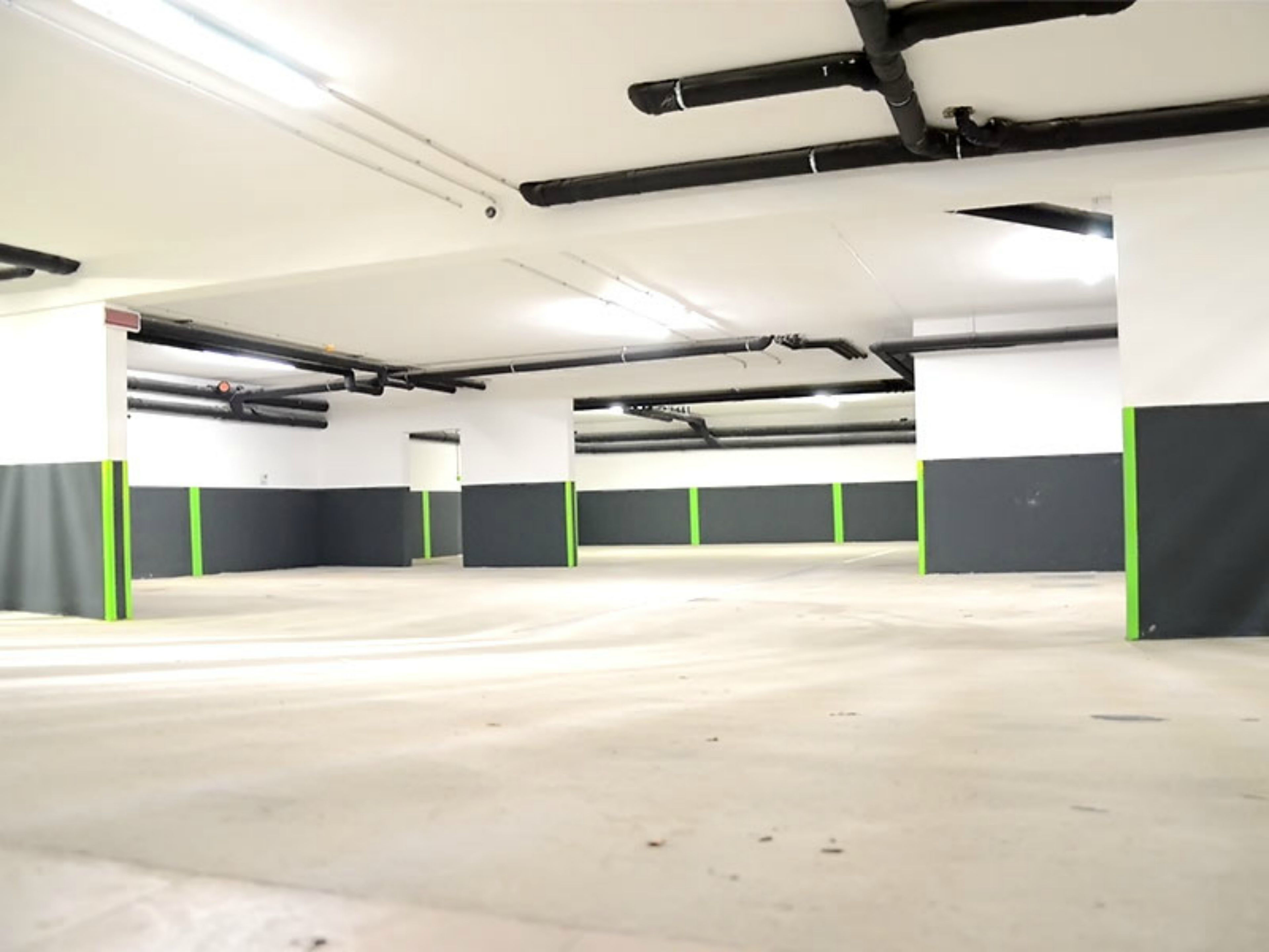 A spacious indoor parking area with concrete floors and white walls, featuring green and black pillars.