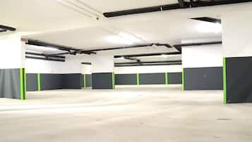 Un amplio estacionamiento interior con pisos de concreto y paredes blancas, que cuenta con pilares verdes y negros.