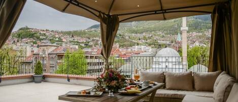 Una terrazza con un tavolo apparecchiato per la colazione, un divano in vimini e vista su una città con edifici e una moschea.
