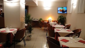 Un restaurant avec plusieurs tables, des chaises et un écran de télévision fixé au mur.