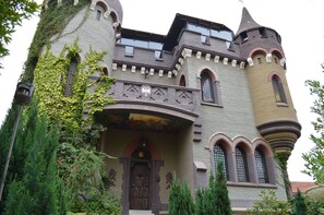 Um edifício semelhante a um castelo, com torre, janelas em arco e paredes cobertas de hera.