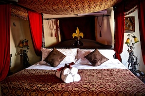 Una cama con una colcha estampada, dos almohadas marrones y una toalla blanca con lazo rojo.