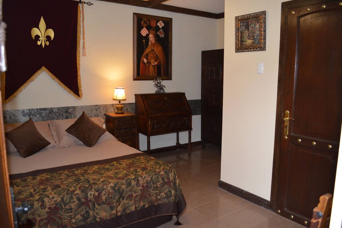 A bedroom with a bed, a nightstand, a lamp, a wooden dresser, and a door.