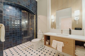 A bathroom with a glass-enclosed shower, a toilet, a sink with a mirror, and a vanity with towels.