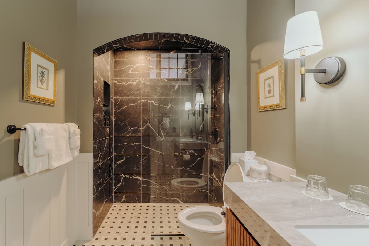 A bathroom with a marble shower, a toilet, a sink with a mirror, and a towel rack.