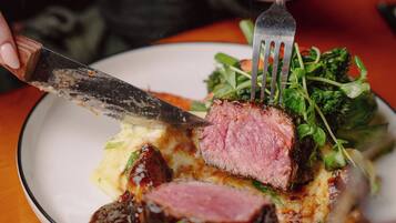Une personne tenant une fourchette et un couteau, coupant un morceau de viande dans une assiette, avec une salade en accompagnement.