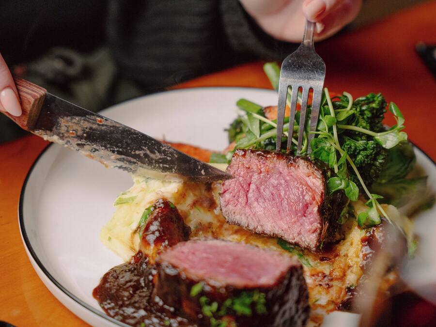 A person holding a fork and knife, cutting a piece of meat from a plate with a side salad.
