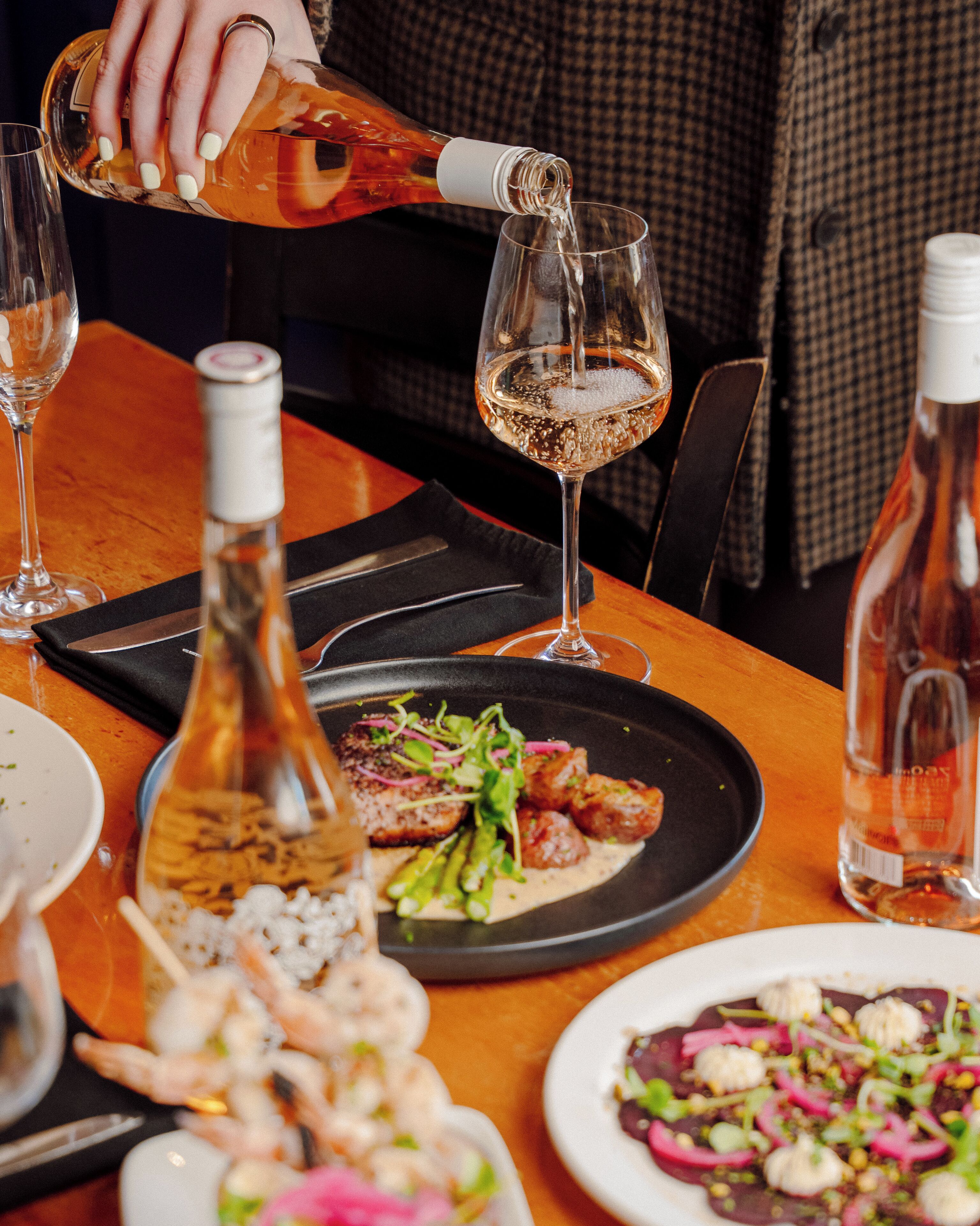 A dining table with plates of food, a bottle of wine, and a glass being filled.