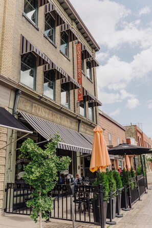 A brick building with a sign reading 'Foster's Inn.' There are outdoor tables and chairs, and a row of potted plants along the sidewalk.