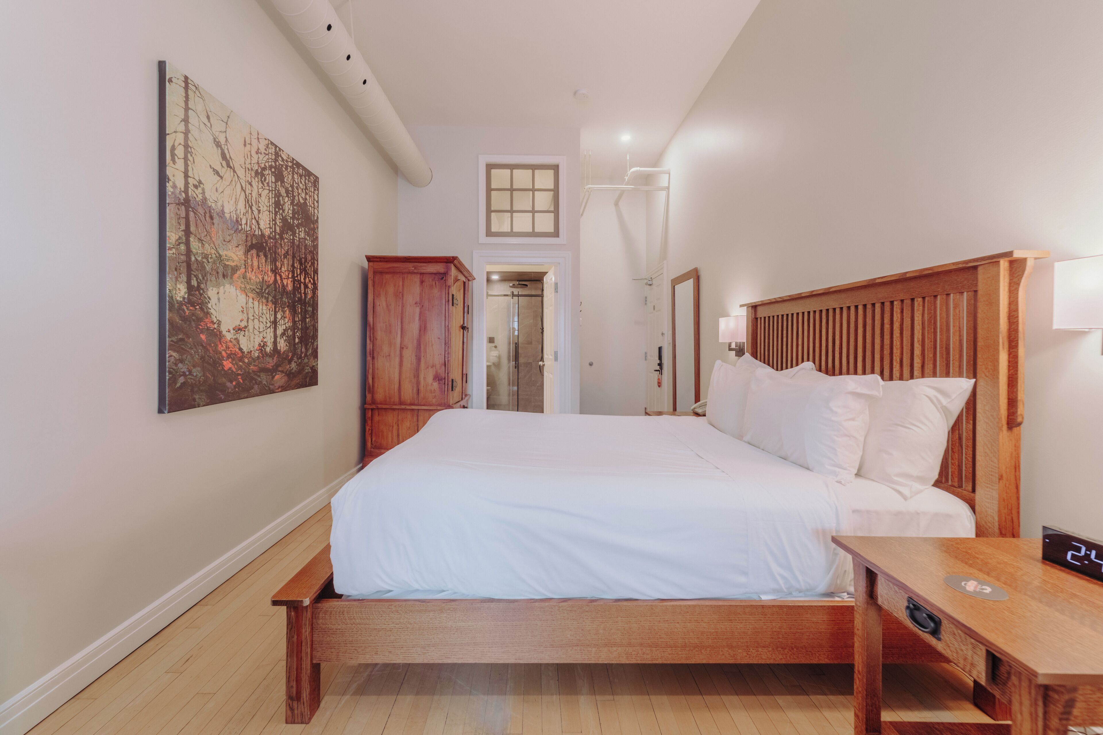 A bedroom with a wooden bed, a nightstand, a wall-mounted lamp, and a painting.