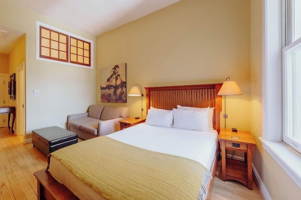 A hotel room with a large bed, two bedside tables, a chair, a small table, and a window.