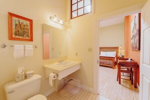 Classic bathroom with a toilet, sink, and mirror, connecting to a cozy bedroom area with a bed and small table.