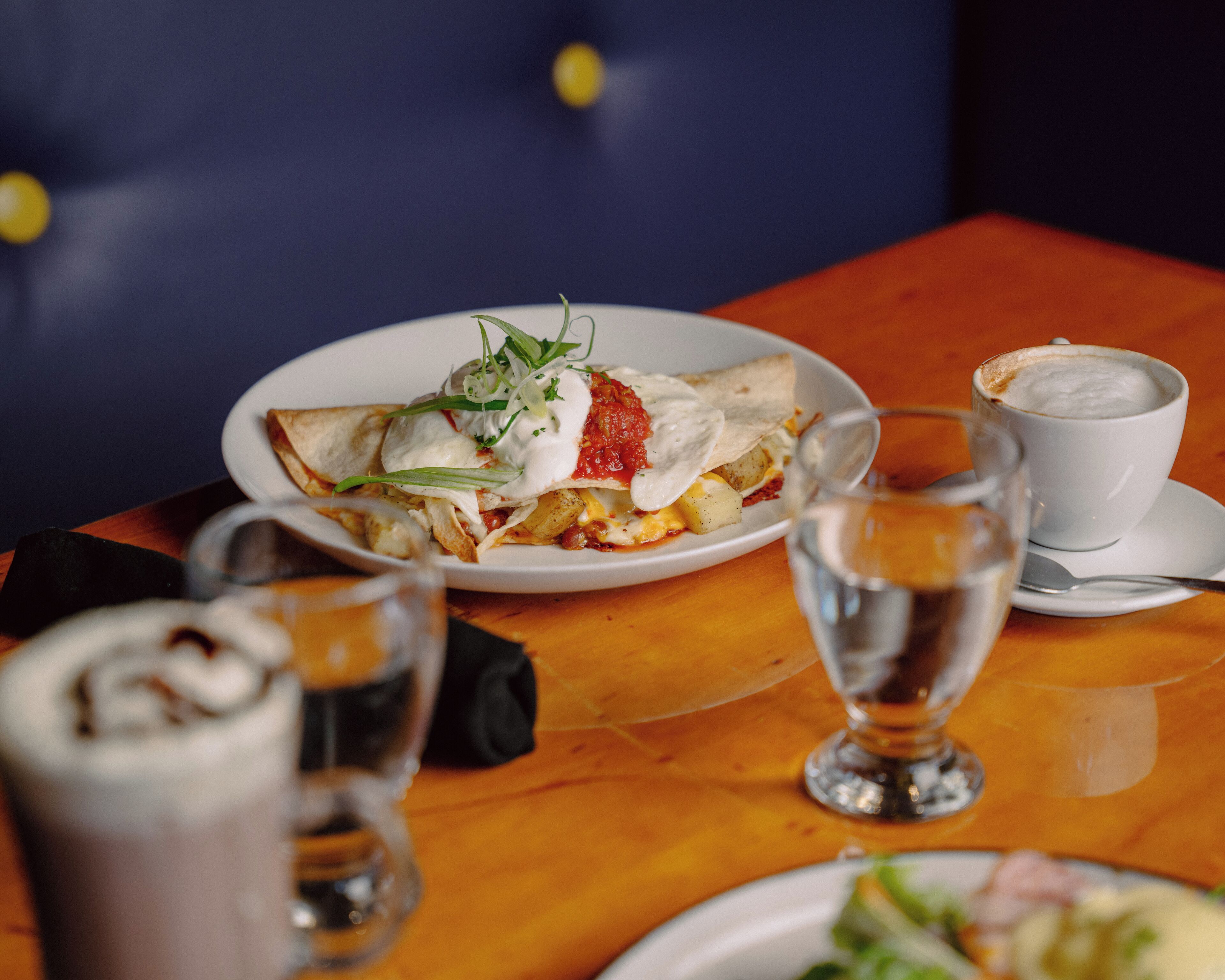 A dining table with plates of food, a cup of coffee, and a glass of water.