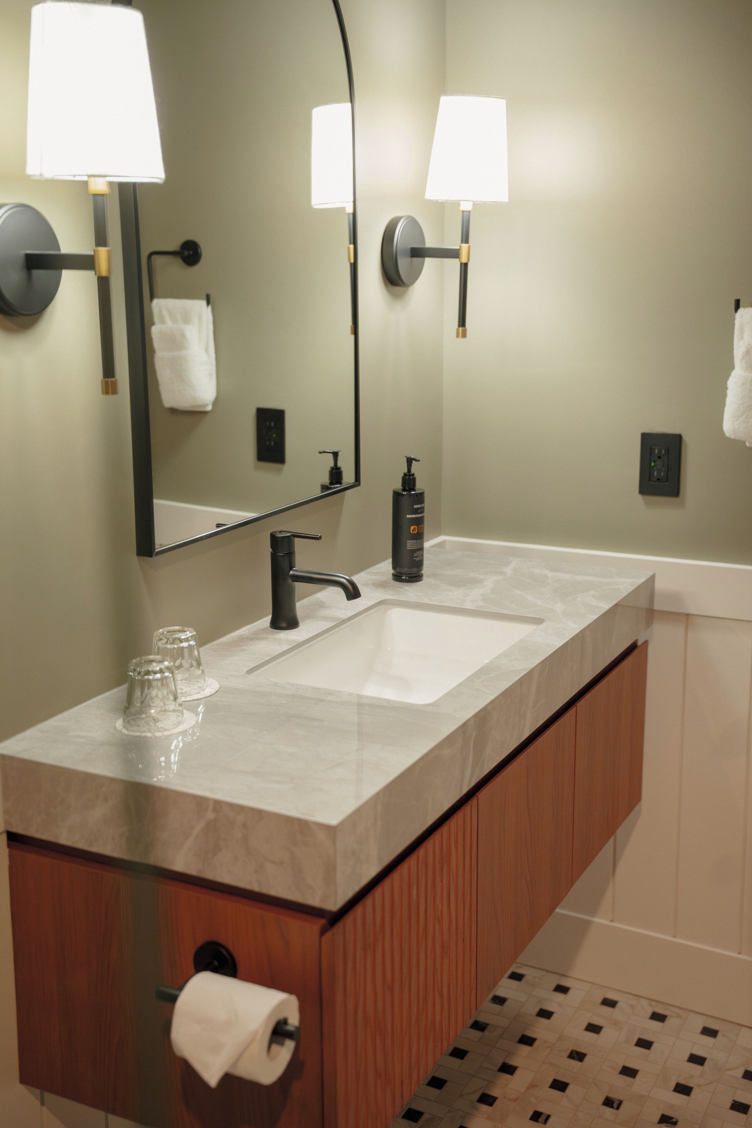A modern bathroom with a marble sink, two wall-mounted lamps, a mirror, and a towel rack.